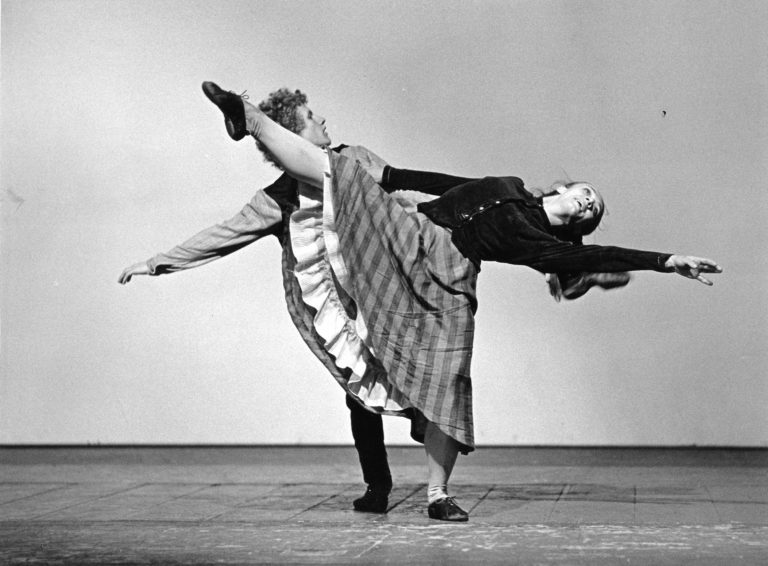 Kaksi tanssijaa, mies ja nainen. Mies pitää kiinni naisesta, joka ojentaa kättään ja vastakkaista jalkaansa.